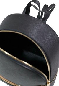 Sac à dos en simili cuir noir avec une forme arrondie, présentant une fermeture éclair dorée et deux bretelles. L'intérieur est en tissu noir sans compartiments visibles.