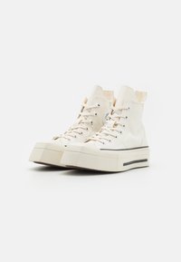 Adidași albi tip high-top cu o talpă platfomitată groasă, din material de pânză de bumbac, cu o bandă de accent neagră aproape de talpă. Prezintă detalii cu gromete.