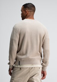 Beiger gestrickter Pullover mit geripptem Muster, lockerer Passform und langen Ärmeln. Verfügt über einen Rundhalsausschnitt und ein dezentes Logo-Tag am Saum.