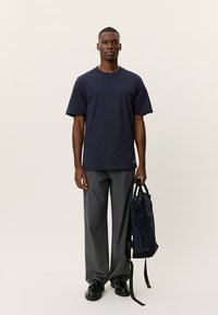 Βαμβακερό μπλε ναυτικό T-shirt με κοντά μανίκια, συνδυασμένο με γκρι παντελόνια με φαρδιές φάσεις και υφασματισμένο μαύρο καρό σακίδιο πλάτης. Μαύρα παπούτσια ολοκληρώνουν το σύνολο.