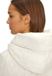 Hellegraue, strukturierte Stoff-Hoodie mit einem weichen, cremefarbenen Fleece-Futter in der Kapuze. Verfügt über einen weiten Kragen und kontrastierende Nähte.