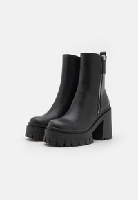 Bottines en cuir noir avec un talon épais, une plateforme épaisse et une fermeture éclair sur le côté. Semelle nervurée pour une meilleure adhérence. Fini lisse.