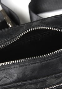 Borsa in tessuto nero con superficie strutturata, scomparti multi-zip e dettagli in metallo argentato. Include una tracolla resistente.