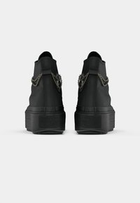 Melnas augstās tenisa kurpes ar teksturētu apdari, ar metāla ķēdes akcentiem un melnu platformas zoli. Converse logo redzams uz papēža.