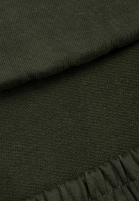 Ciemo zielona tkanka z bliska, prezentująca złożoną strukturę dzianiny oraz szczegóły elastycznego pasa.