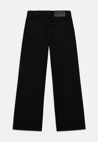 Schwarze Denim-Hosen mit weiter Beinweite, die eine glatte Textur aufweisen, zwei Gesäßtaschen und einen Bund mit einem Logo-Patch auf der Rückseite haben.