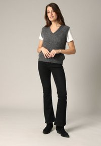 Gilet en tricot gris avec un col en V et des manches courtes, porté sur un t-shirt blanc. Associé à un jean noir évasé et des bottines noires.