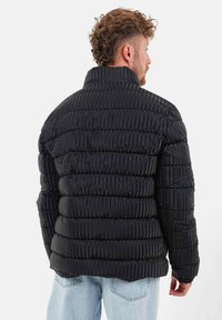 Zwarte pufferjack met een gestructureerd, gestikt ontwerp. Voorzien van een hoge kraag en ribbelsteken. Reflecterend materiaal verbetert de visuele details.