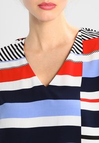 Multikleurige blouse met V-hals, met horizontale strepen in rood, blauw, wit en zwart. Soepele stof met variërende strookbreedtes.