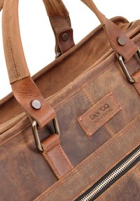 Bruine leren tas met een gladde afwerking, voorzien van stevige metalen hardware, twee handvatten bovenaan en een ritscompartiment. Opvallend merklabel inbegrepen.