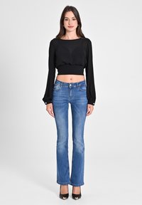 Schwarzes, langärmeliges, kurzes Oberteil mit rundem Halsausschnitt; kombiniert mit hellblauen weiten Jeans und schwarzen High Heels mit metallischen Akzenten.