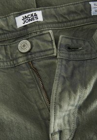 Prim-plan cu talia blugilor verzi Jack & Jones cu nasture metalic, fermoar parțial deschis și etichetă vizibilă a mărcii.