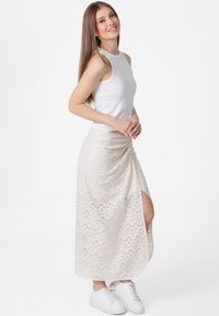 Een witte tanktop gecombineerd met een crèmekleurige maxi-jurk met patroon en een zijsplit, gedragen met witte sneakers.