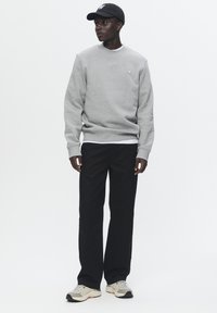 Gray sweatshirt with a round neck and a small logo, paired with black pants. Man wears a black cap and beige sneakers with gray accents.