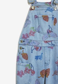 Pettorina in denim azzurro chiaro con stampa floreale e di frutta in tonalità di rosa, viola e rosso. Include dettagli in metallo argentato e più tasche.