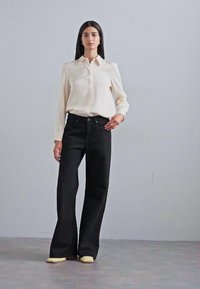 Cream satin shirt with a collar, paired with high-waisted black wide-leg pants and light-colored shoes on a gray background.