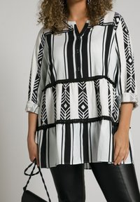 Tunique rayée noir et blanc avec des motifs géométriques, patte de boutonnage et volants. Associée à des leggings noirs et un petit sac.