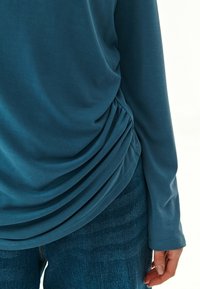 Teallin pitkähihaisessa paidassa on kerrottu sivuseikkailu, ja se on valmistettu pehmeästä kankaasta. Yhdistetty teksturoituihin sinisiin farkkuihin, jotka tarjoavat rentoa istuvuutta ja sileää viimeistelyä.