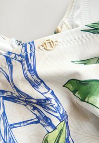 Blumiger Badeanzugstoff mit hellem Hintergrund, grünen Blättern und blauen Zweigillustrationen. Mit Detail eines goldfarbenen Verschlusses.