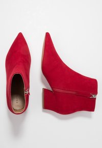 Czerwone zamszowe botki za kostkę z wydłużonym noskiem i skromnym obcasem na koturnie. Posiadają zapięcie na zamek błyskawiczny po boku oraz gładkie wykończenie wewnętrzne.