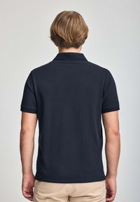 Svart polotröja med en klassisk design, med krage och korta ärmar. Slät textur, jämnt stickad tyg. Inga synliga logotyper eller mönster.