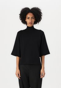 Svart turtleneck med korte, brede ermer og en avslappet passform, laget av et mykt stoff, stylet med svarte bukser.