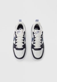 O pereche de sneakers Nike negri și albi cu logo-uri swoosh albastre și șireturi albe, văzuți de sus pe un fundal simplu.