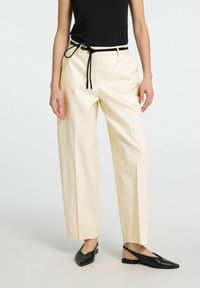 Gräddfärgade, vida byxor med hög midja och svart dragsko-bälte, parat med svarta, spetsiga slingback-lägenheter.