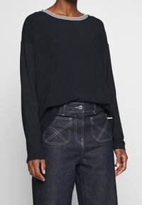 Svart långärmad topp med vitrandig halsringning, tillsammans med mörka denimjeans med kontrasterande sömmar och hög midja.