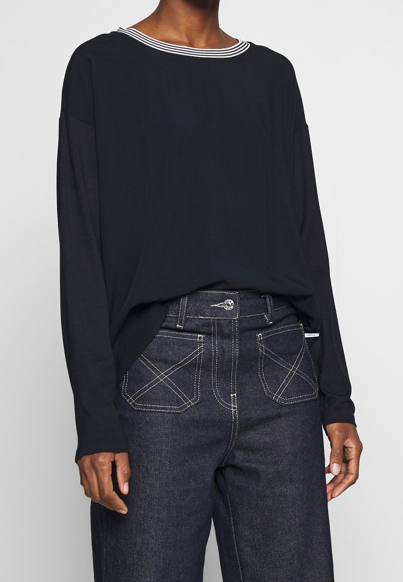 Svart långärmad topp med vitrandig halsringning, tillsammans med mörka denimjeans med kontrasterande sömmar och hög midja.