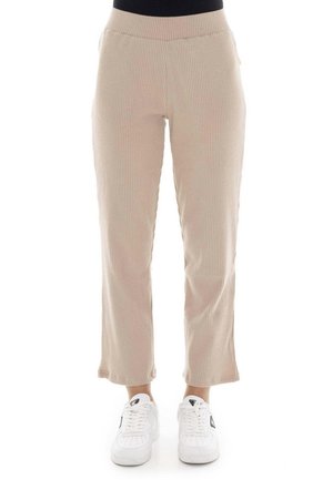 Modèle portant un pantalon beige côtelé à jambes droites et des baskets blanches sur fond blanc.