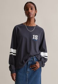 Langsleeve donkergrijze shirt met witte strepen op de mouwen en een grafisch cijfer "15" op de voorkant. Zachte stof, comfortabele pasvorm, casual stijl.