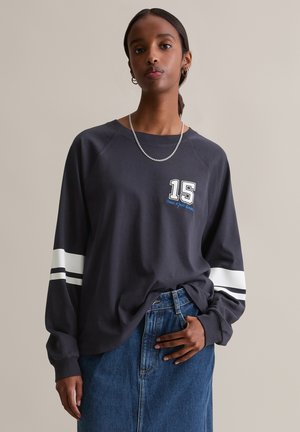 Langärmliges, dunkelgraues Shirt mit weißen Streifen an den Ärmeln und einer grafischen Zahl "15" auf der Vorderseite. Weicher Stoff, lässige Passform, lockerer Stil.