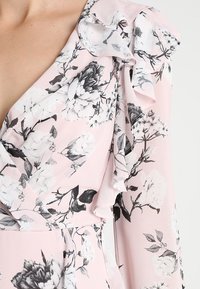 Abito floreale rosa con stampa di fiori in bianco e nero, dettagli arricciati sulle spalle e un tessuto leggero e fluido.