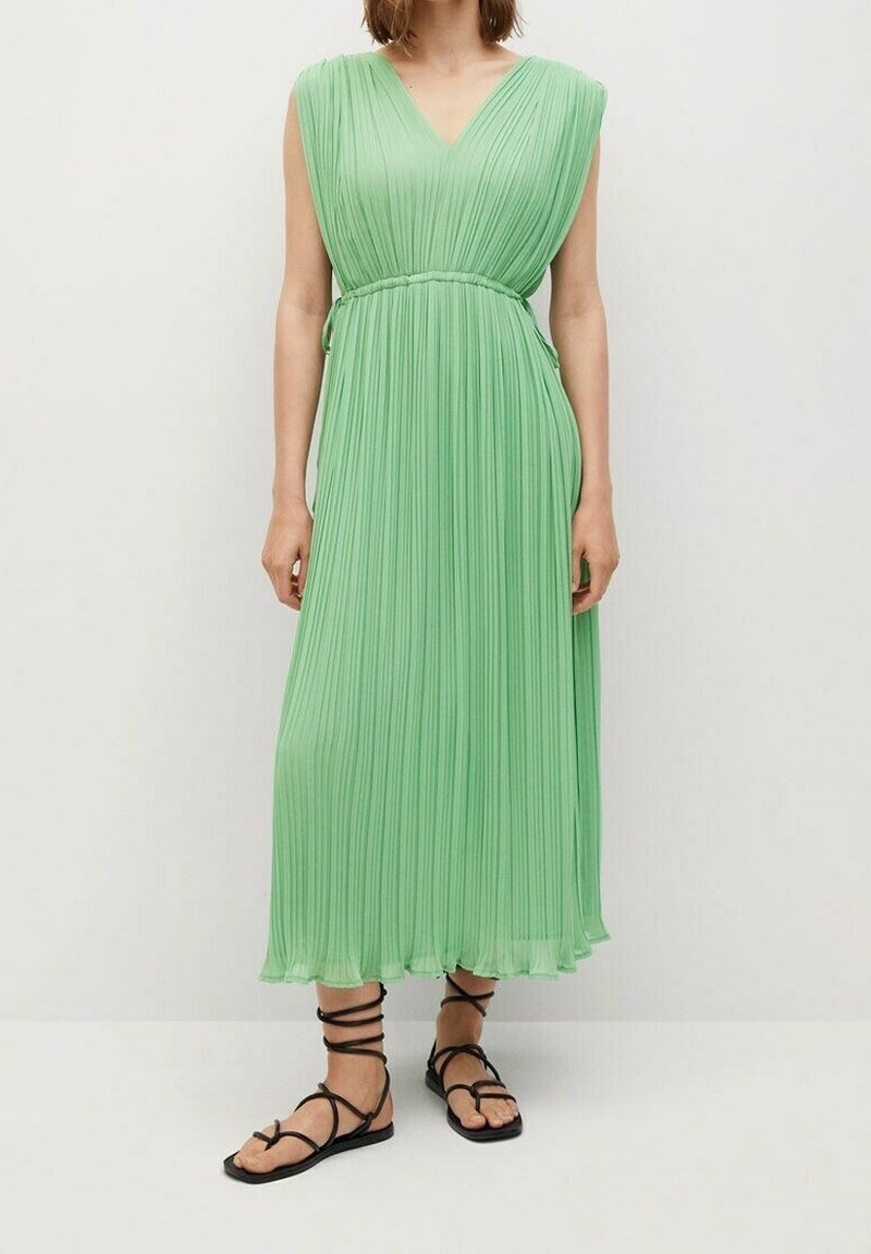 Vestido midi plisado verde con escote en V, hombros anchos y detalle de cintura atada, combinado con sandalias negras de tiras.