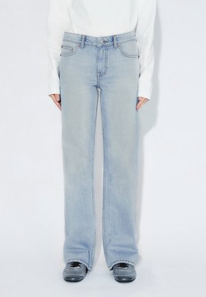 Lyseblå jeans med vide ben og høj talje, fem-lomme design og subtil falmen. Kombineret med grå sneakers og en hvid langærmet skjorte.