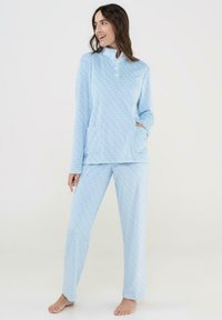 Conjunto de pijama azul claro que presenta una parte superior con cuello y tres botones, dos bolsillos frontales, y pantalones a juego decorados con un sutil patrón de lunares.