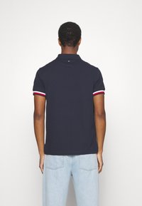 Donkerblauwe polo met korte mouwen, voorzien van rode en witte gestreepte accenten op de mouwen. Klassiek kraagontwerp met een gestructureerde stof.