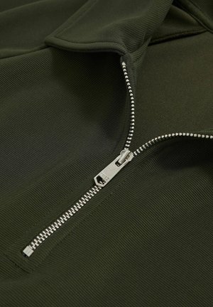 Pulover verde închis cu închidere prin fermoar. Tesătură texturată cu un model de nervuri. Fermoar argintiu vizibil de-a lungul deschiderii.