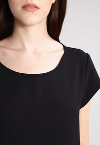 Černý top vyrobený z hladké tkaniny, s kulatým výstřihem a krátkými rukávy, s přiléhavým střihem a jemnou texturou.