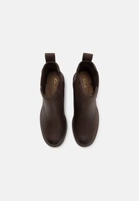 Botas de cuero marrón hasta el tobillo con paneles laterales elásticos, punteras redondeadas y detalles de costura. Presentan un logo en el interior y tiradores para facilitar el uso.