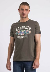 T-shirt en coton vert olive à manches courtes, avec l'inscription "HONOLULU RIDE THE WAVES" imprimée en blanc et un graphique de planche de surf coloré.