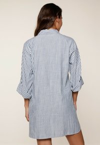 Vestido camisero a rayas en azul y blanco, con cuello, mangas enrolladas y un corte relajado que termina por encima de la rodilla.