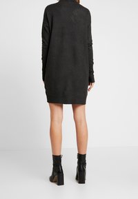 Tmavě šedé pletené šaty, do délky po stehna, s dlouhými rukávy a ribbed manžetami. Vybavené černými kotníkovými botami s blokovým podpatkem.