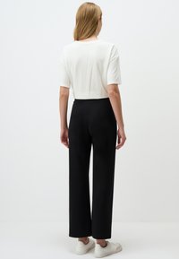 T-shirt cropped bianco in cotone abbinato a pantaloni neri a gamba larga, con una texture morbida e una cintura elastica. Sneakers bianche completano il look.
