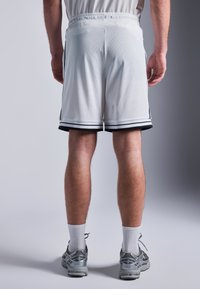 Biele sieťované basketbalové šortky s čiernymi bočnými prúžkami a elastickým pásom, ktoré majú voľný strih a dĺžku po kolená.