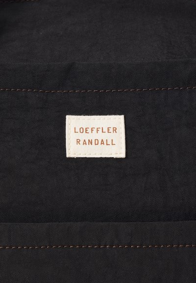 Black fabric with a stitched label reading "LOEFFLER RANDALL" in white and rust, featuring a rectangular shape and textured finish.
