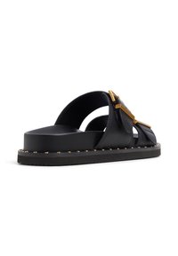 Sandalo in pelle nera con larghe cinghie e dettagli in metallo dorato. Caratterizzato da una suola spessa e texturizzata con borchie metalliche attorno ai bordi.