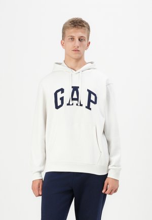 White hooded sweatshirt made of soft fabric featuring a navy "GAP" logo, kangaroo pocket, and ribbed cuffs with a relaxed fit.