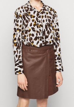 Leopardprint blouse in beige, bruin en gele tinten, gecombineerd met een bruin leren minirok met een zijzak en een gestroomlijnd ontwerp.